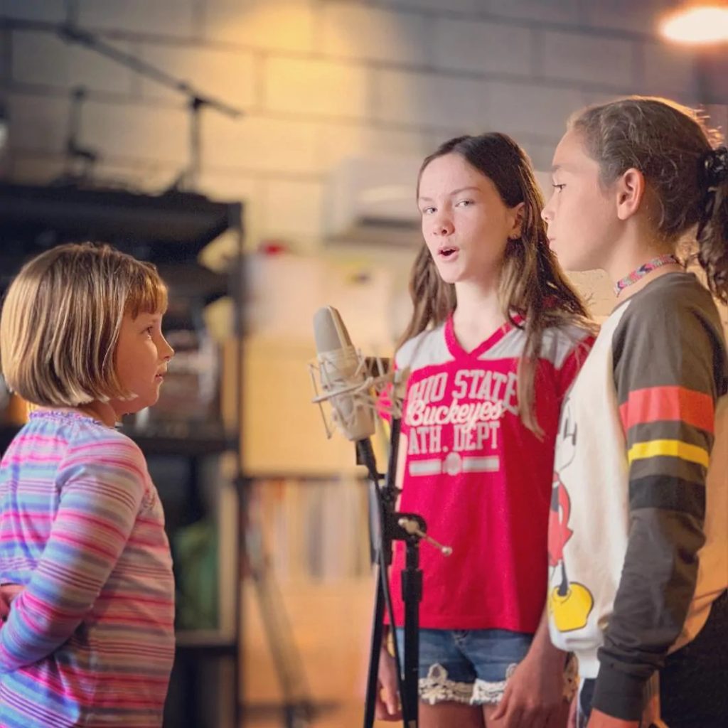 A group of young girls singing around a microphone